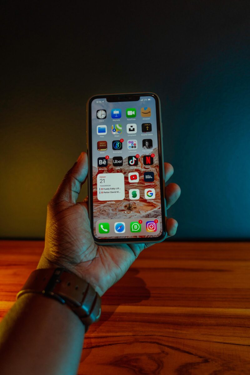 A hand holding a smartphone displaying app icons, with a modern minimalistic background.